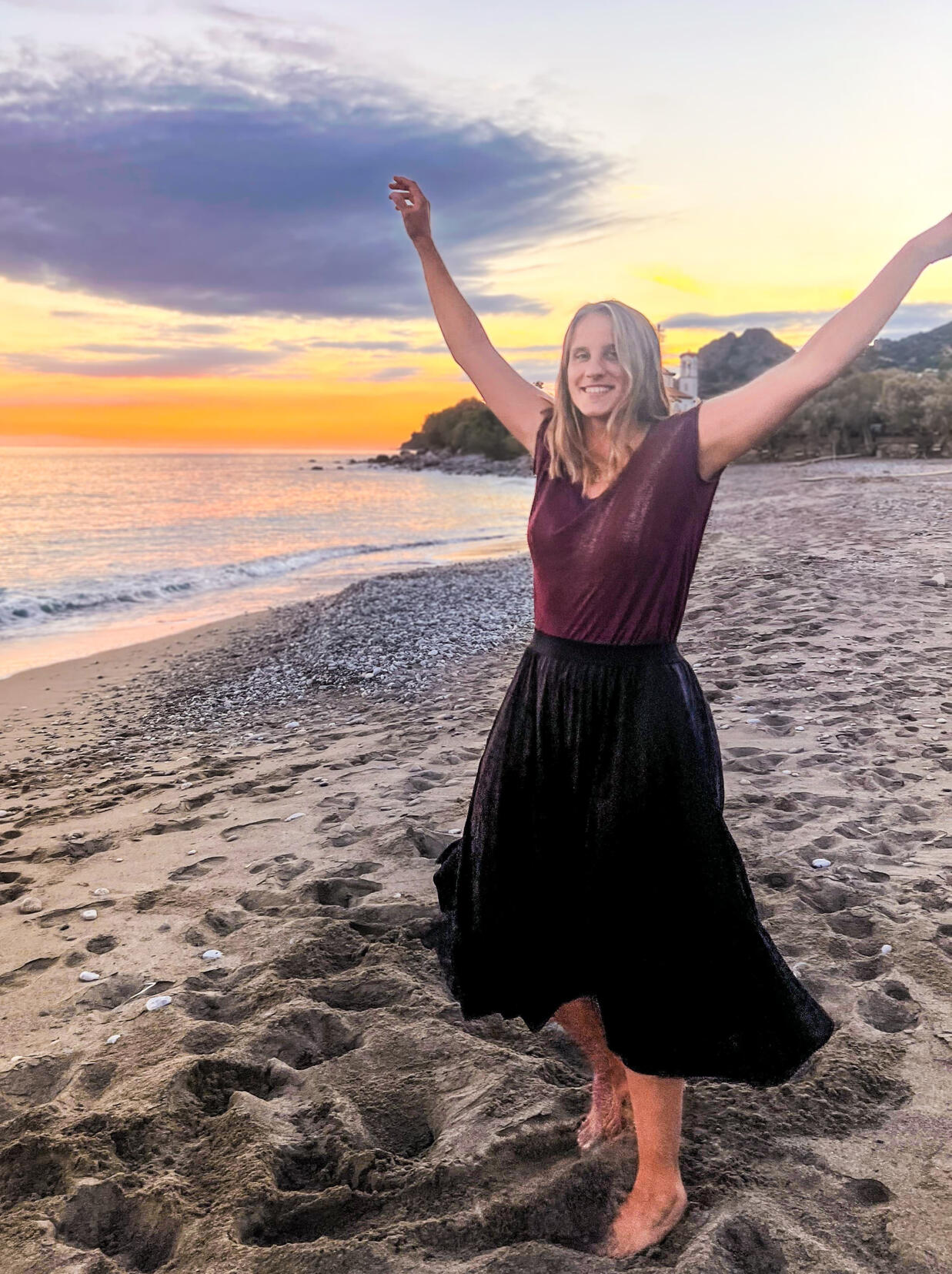 Daniela Kellner mit ausgestreckten Armen am Strand bei Sonnenuntergang.